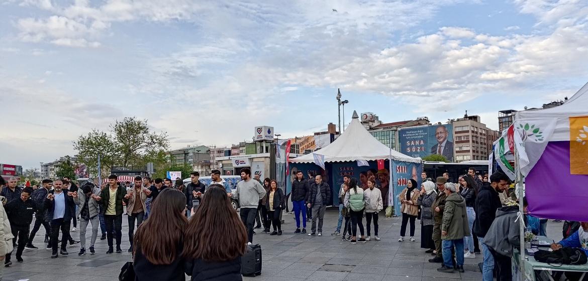 Wahlkampf 2023: Im Vordergrund tanzen Menschen vor dem Stand der Yeşil Sol Partei. Im Hintergrund ist Kemal Kılıçdaroğlu auf einer Hauswand zu sehen. Foto: Kinan Alzouabi