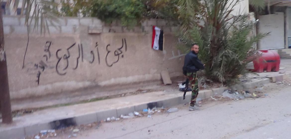 Ein Milizenkämpfer des Regimes steht Wache am Ortseingang des Damaszener Vorortes Moadamiya. Bashar al-Assads Truppen hungerten Moadamiya systematisch aus, wie auch das Graffiti an der Wand besagt: "Hunger oder Niederknien." Der Medienaktivist Qusai Zakarya hat das Foto aus einiger Entfernung gemacht und uns zur Verfügung gestellt (C).