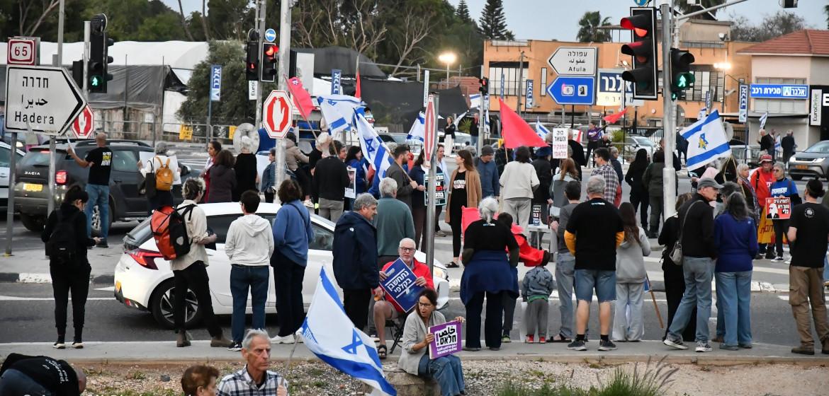 Versammlung an der Karkur-Kreuzung. Eine Demonstrantin hält ein Schild mit der Aufschrift „Schluss mit dem endlosen Krieg” auf Hebräisch und Arabisch in den Händen. Foto: Amos Gil Photographer.