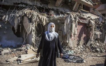 Auch die Stadt Cizre im Osten der Türkei wurde in großen Teilen von der türkischen Armee zerstört. Das Bild zeigt eine Frau vor den Trümmern ehemaliger Wohnhäuser, März 2016. Foto: "Cizre çatışmaları sırasında hasar gören bina ve bir Cizreli kadın, 2 Mart 2016" von Nedim Yılmaz/Flickr (https://flic.kr/p/LnpD53), Lizenz: cc-by sa 2.0 (https://creativecommons.org/licenses/by-sa/2.0/)