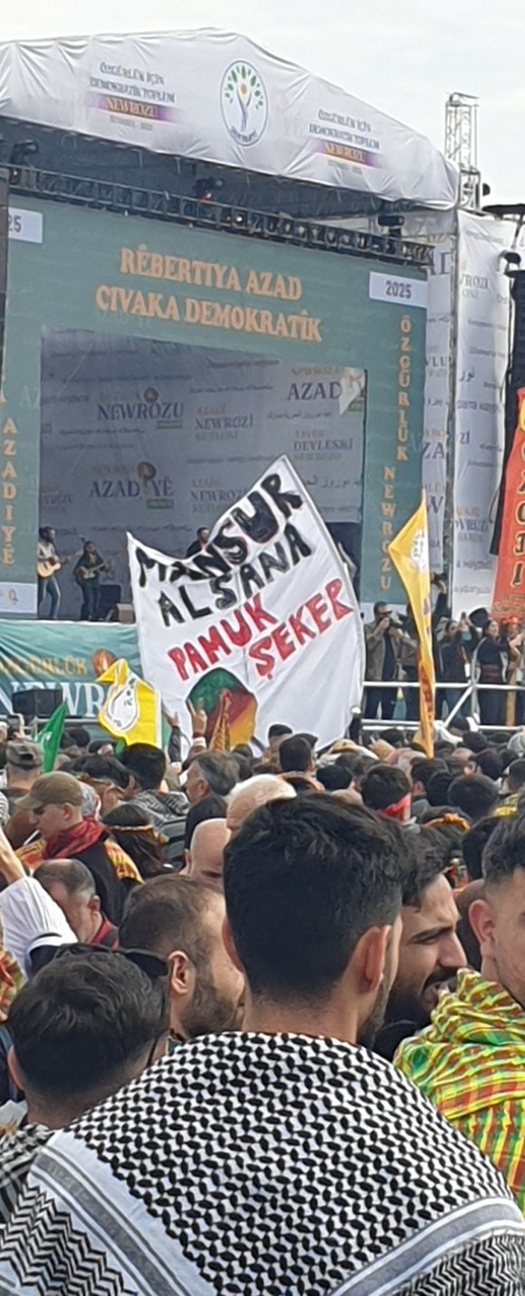 Newrozfeiernde in Istanbul 2025, die ein Transparent hochhalten, auf dem “Mansur, kauf’ doch Zuckerwatte!” steht. Foto: Filiz Yildirim.
